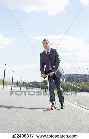 Businessman looking away while riding scooter on street View Large Photo Image Stock Photo - Businessman looking away while riding scooter on street. Fotosearch