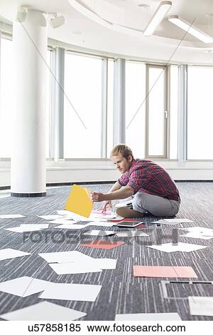 Stock Photography - Businessman organizing photographs while sitting on floor at creative office. Fotosearch