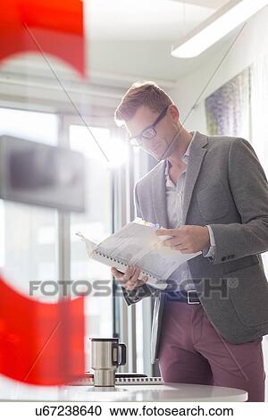 Stock Image - Businessman reading file in creative office. Fotosearch