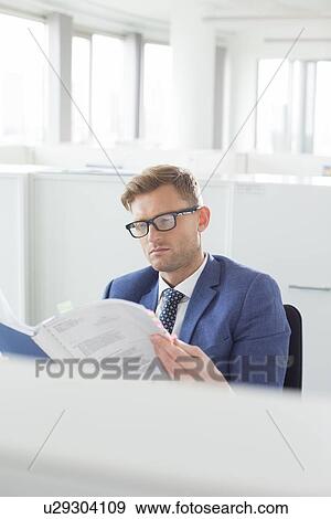 Stock Photo - Businessman reading file in creative office. Fotosearch