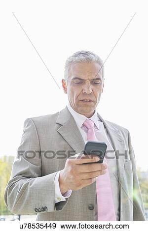 Stock Photo - Businessman reading text message on cell phone against sky. Fotosearch