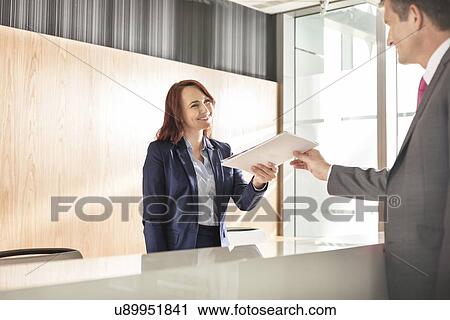 Businessman receiving document from receptionist in office View Large Photo Image Stock Image - Businessman receiving document from receptionist in office. Fotosearch