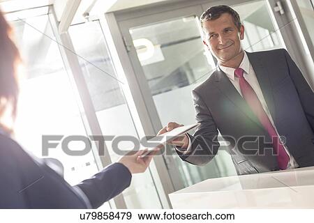 Stock Photo - Businessman receiving document from receptionist in office. Fotosearch