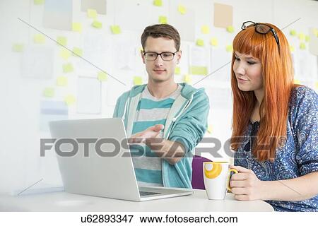 Stock Photo - Businessman showing something to female colleague on laptop in creative office. Fotosearch