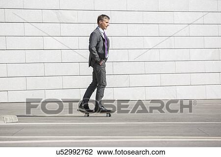 Stock Image - Businessman skateboarding on street. Fotosearch