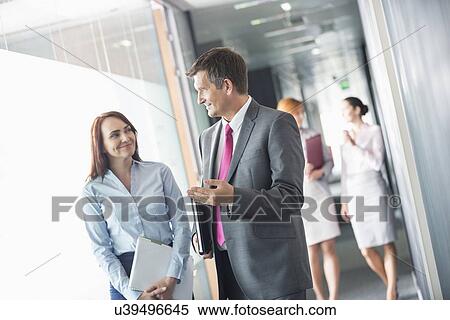 Businessman talking with female colleague while walking in office corridor View Large Photo Image Stock Photography - Businessman talking with female colleague while walking in office corridor. Fotosearch