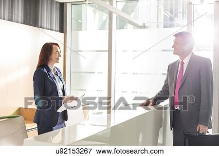 Stock Photo - Businessman talking with receptionist in office. Fotosearch