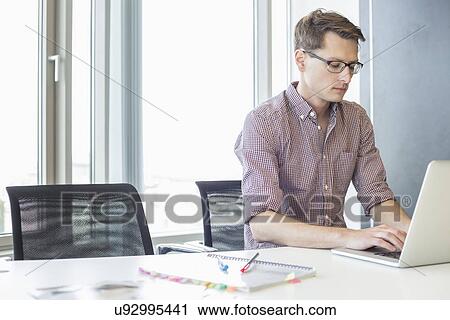 Stock Image - Businessman using laptop at desk in creative office. Fotosearch