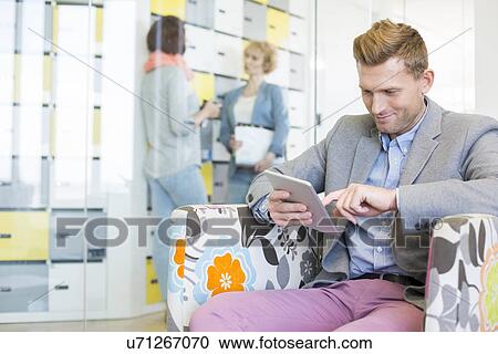 Businessman using tablet PC with colleagues discussing in background at creative office View Large Photo Image Stock Image - Businessman using tablet PC with colleagues discussing in background at creative office. Fotosearch