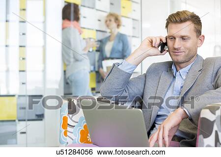 Stock Photograph - Businessman using technologies with colleagues discussing in background at creative office. Fotosearch