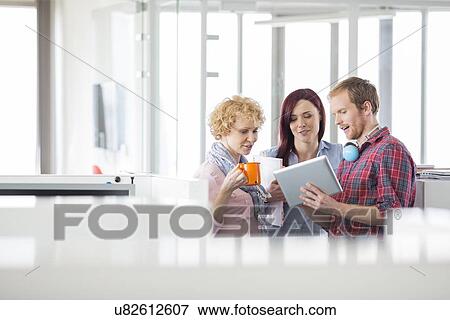 Stock Photo - Businessman with female colleagues discussing over tablet PC in office. Fotosearch