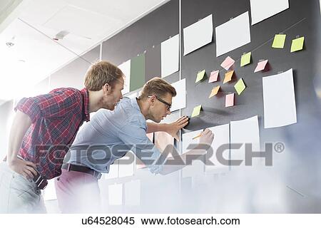 Businessmen analyzing documents on wall in office View Large Photo Image Stock Photography - Businessmen analyzing documents on wall in office. Fotosearch