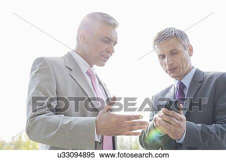 Businessmen discussing over mobile phone outdoors View Large Photo Image Stock Photography - Businessmen discussing over mobile phone outdoors. Fotosearch