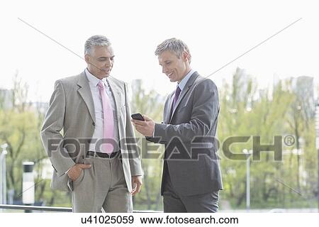 Stock Photo - Businessmen using cell phone together outdoors. Fotosearch