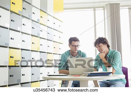 Stock Image - Businessmen using laptop at table in locker room at creative office. Fotosearch