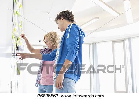 Businesspeople analyzing document stuck on wall in creative office View Large Photo Image Stock Photo - Businesspeople analyzing document stuck on wall in creative office. Fotosearch