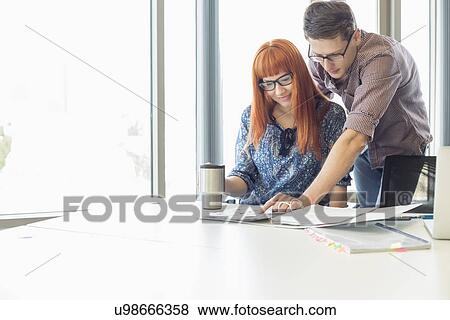 Businesspeople analyzing file together at desk in creative office View Large Photo Image Stock Photo - Businesspeople analyzing file together at desk in creative office. Fotosearch