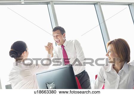 Stock Image - Businesspeople celebrating success in office. Fotosearch