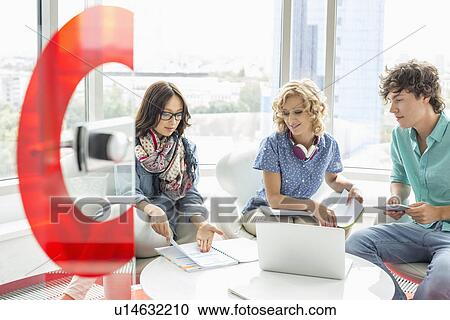 Stock Image - Businesspeople discussing over file in creative office. Fotosearch