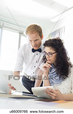 Businesspeople discussing over samples at desk in creative office View Large Photo Image Stock Photograph - Businesspeople discussing over samples at desk in creative office. Fotosearch