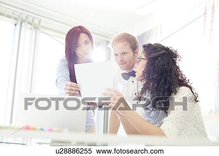 Businesspeople discussing over photograph in creative office View Large Photo Image Stock Photography - Businesspeople discussing over photograph in creative office. Fotosearch