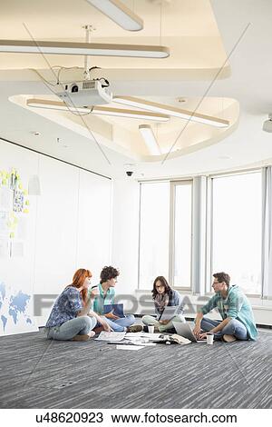 Businesspeople discussing while sitting on floor in creative office View Large Photo Image Stock Image - Businesspeople discussing while sitting on floor in creative office. Fotosearch
