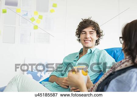 Businesspeople having coffee while relaxing on beanbag chairs in creative office View Large Photo Image Stock Photo - Businesspeople having coffee while relaxing on beanbag chairs in creative office. Fotosearch