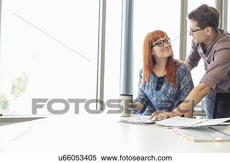 Businesspeople looking at each other while working at desk in creative office View Large Photo Image Stock Photography - Businesspeople looking at each other while working at desk in creative office. Fotosearch