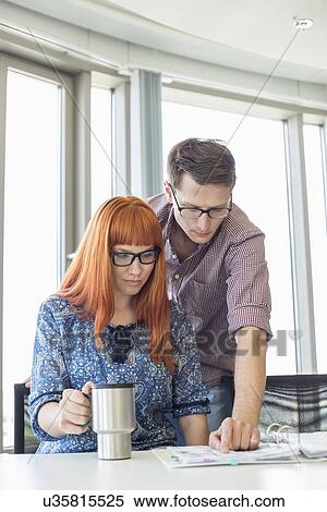 Stock Photography - Businesspeople reading file together at desk in creative office. Fotosearch