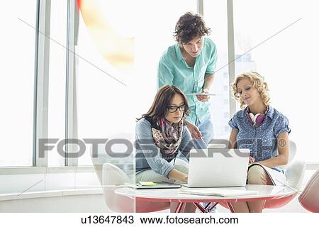 Stock Image - Businesspeople using laptop at table in creative office. Fotosearch