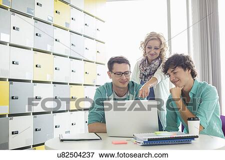 Businesspeople using laptop at table in locker room at creative office View Large Photo Image Stock Photo - Businesspeople using laptop at table in locker room at creative office. Fotosearch