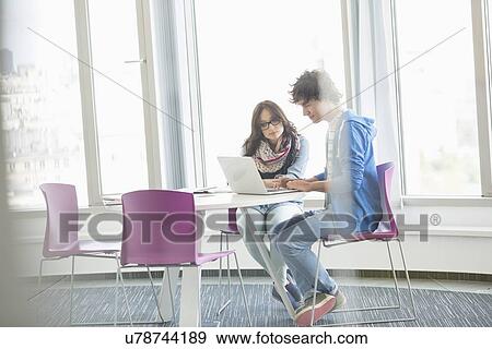 Stock Photo - Businesspeople using laptop together in creative office. Fotosearch