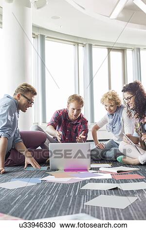 Businesspeople using laptop while sitting on floor at creative office View Large Photo Image Stock Image - Businesspeople using laptop while sitting on floor at creative office. Fotosearch