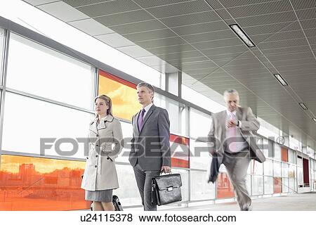 Businesspeople walking while male colleague running in railroad station View Large Photo Image Stock Photo - Businesspeople walking while male colleague running in railroad station. Fotosearch