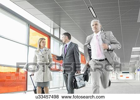 Stock Photo - Businesspeople walking while male colleague running in railroad station. Fotosearch