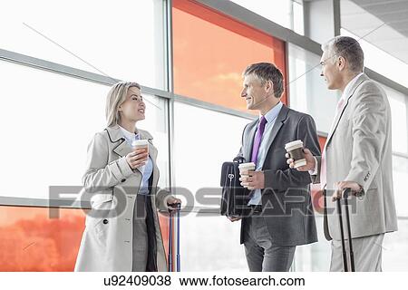 Stock Photo - Businesspeople with coffee cups talking on railroad platform. Fotosearch