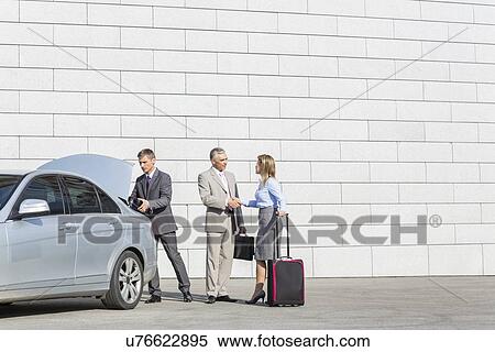 Stock Photography - Businesspeople with luggage shaking hands outside car on street. Fotosearch