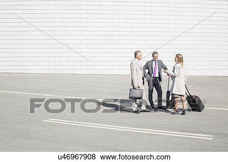 Stock Photo - Businesspeople with luggage communicating on street. Fotosearch