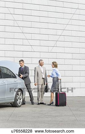Businesspeople with luggage communicating outside car on street View Large Photo Image Stock Photo - Businesspeople with luggage communicating outside car on street. Fotosearch
