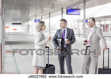 Stock Image - Businesspeople with luggage talking on railroad platform. Fotosearch