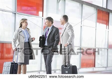 Stock Image - Businesspeople with luggage talking on railroad platform. Fotosearch
