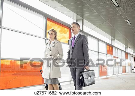 Stock Image - Businesspeople with luggage walking in railroad station. Fotosearch