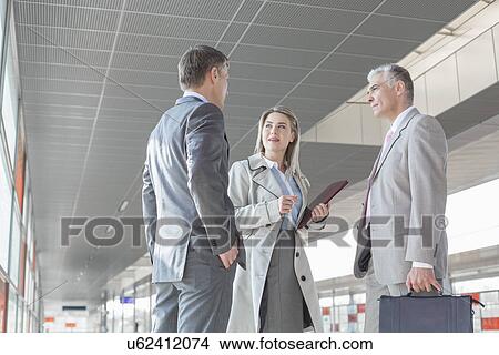 Picture - Businesswoman communicating with male colleagues on train platform. Fotosearch