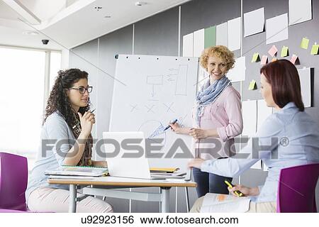 Stock Photograph - Businesswoman explaining pie chart to colleagues in creative office. Fotosearch