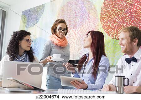 Picture - Businesswoman giving coffee to female colleague in creative office. Fotosearch