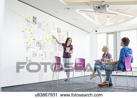 Stock Image - Businesswoman giving presentation to colleagues in creative office space. Fotosearch