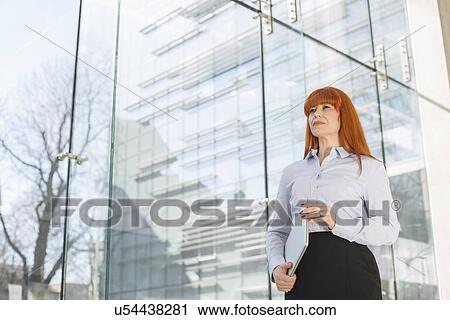 Businesswoman holding laptop by glass wall in office View Large Photo Image Stock Image - Businesswoman holding laptop by glass wall in office. Fotosearch