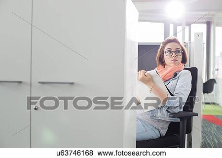 Businesswoman holding notepad while sitting on chair at creative office View Large Photo Image Stock Photo - Businesswoman holding notepad while sitting on chair at creative office. Fotosearch