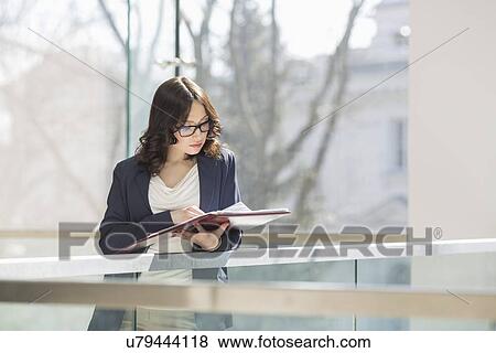 Businesswoman reading documents against railing in office View Large Photo Image Stock Photo - Businesswoman reading documents against railing in office. Fotosearch