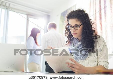 Businesswoman reading notepad at creative office with colleagues in background View Large Photo Image Stock Image - Businesswoman reading notepad at creative office with colleagues in background. Fotosearch